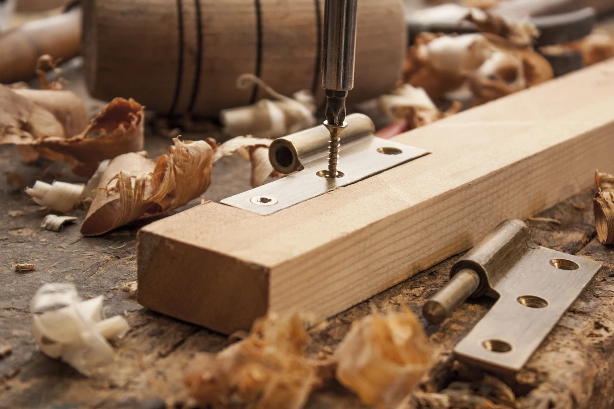 Atelier de menuiserie avec vissage d'une charnière métallique sur pièce de bois massif à l'aide d'une perceuse-visseuse
