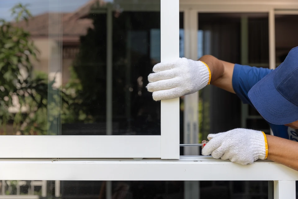 Technicien en tenue professionnelle (polo ou combinaison) descending d'un véhicule utilitaire blanc ou gris, portant sa caisse à outils et équipement de vitrerie/menuiserie. Il se tient à côté d'une fenêtre ou porte de bâtiment résidentiel, prêt à intervenir immédiatement. L'image doit montrer son autonomie et son équipement complet, symbolisant l'intervention rapide et efficace dès le premier passage.