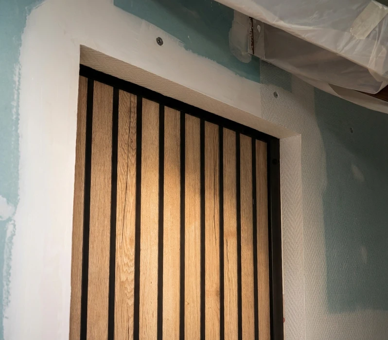 Intérieur d'un appartement sous combles vide, porte coulissante type barn door en bois massif aspect chêne vieilli, montée sur rail métallique noir en applique